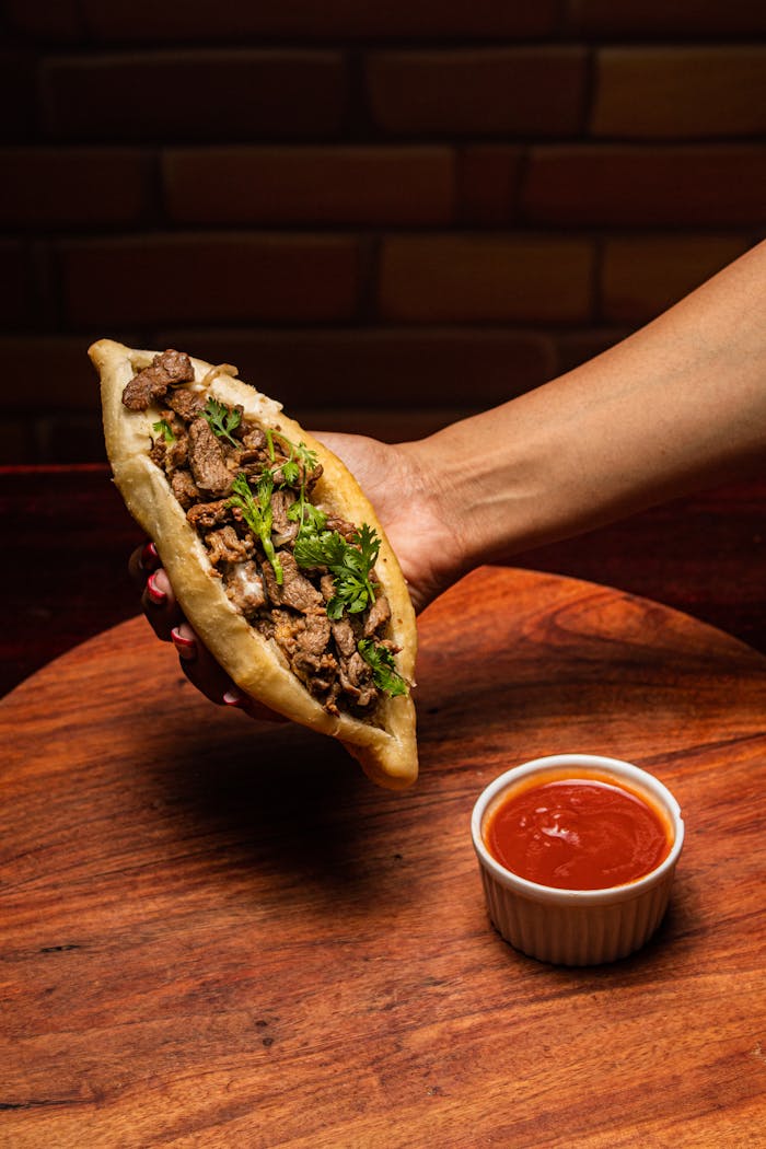 Appetizing shawarma held by hand with a side of spicy sauce, perfect for food lovers.